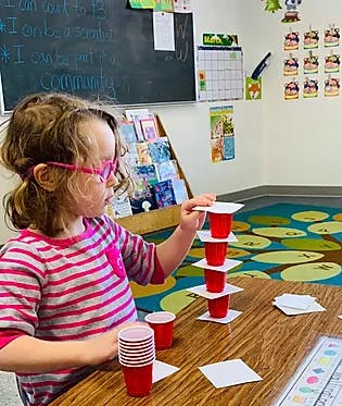 Child stacking red cups and paper squares on a table