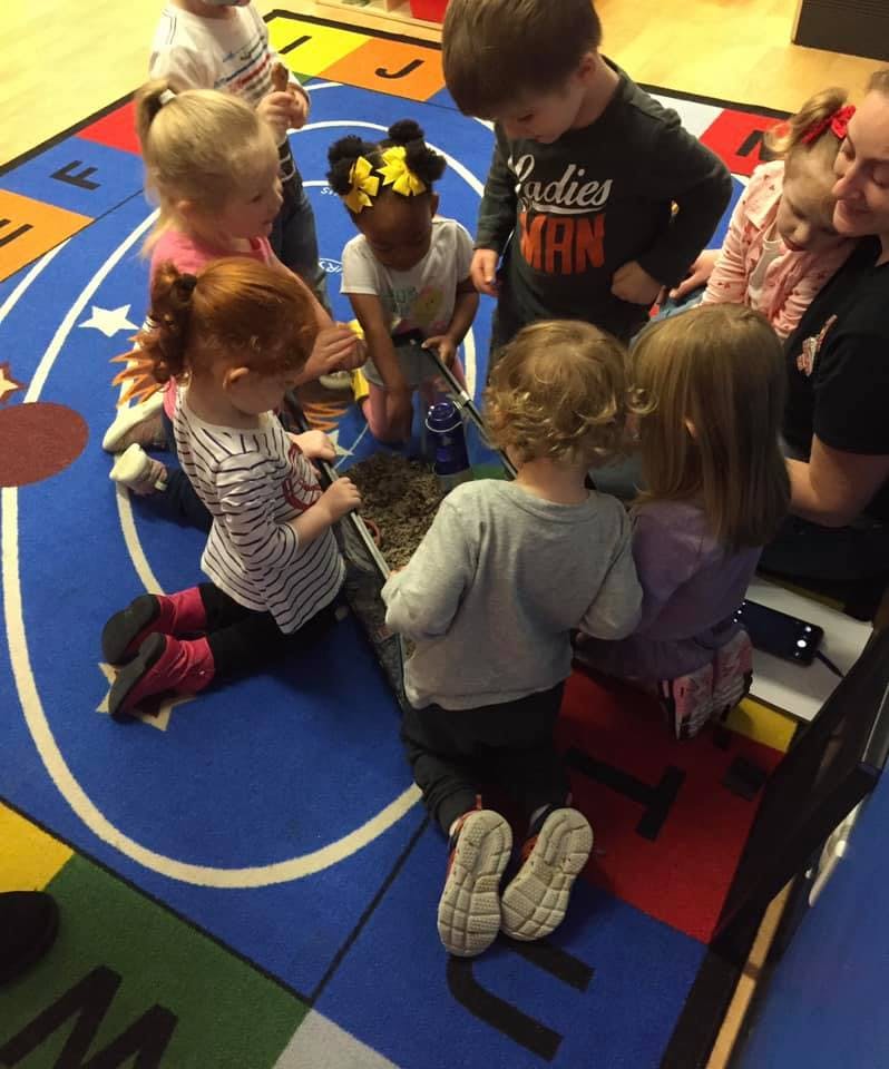 Children gathered around a sensory bin on a colorful rug
