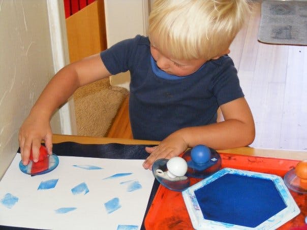 Child stamping blue shapes onto white paper