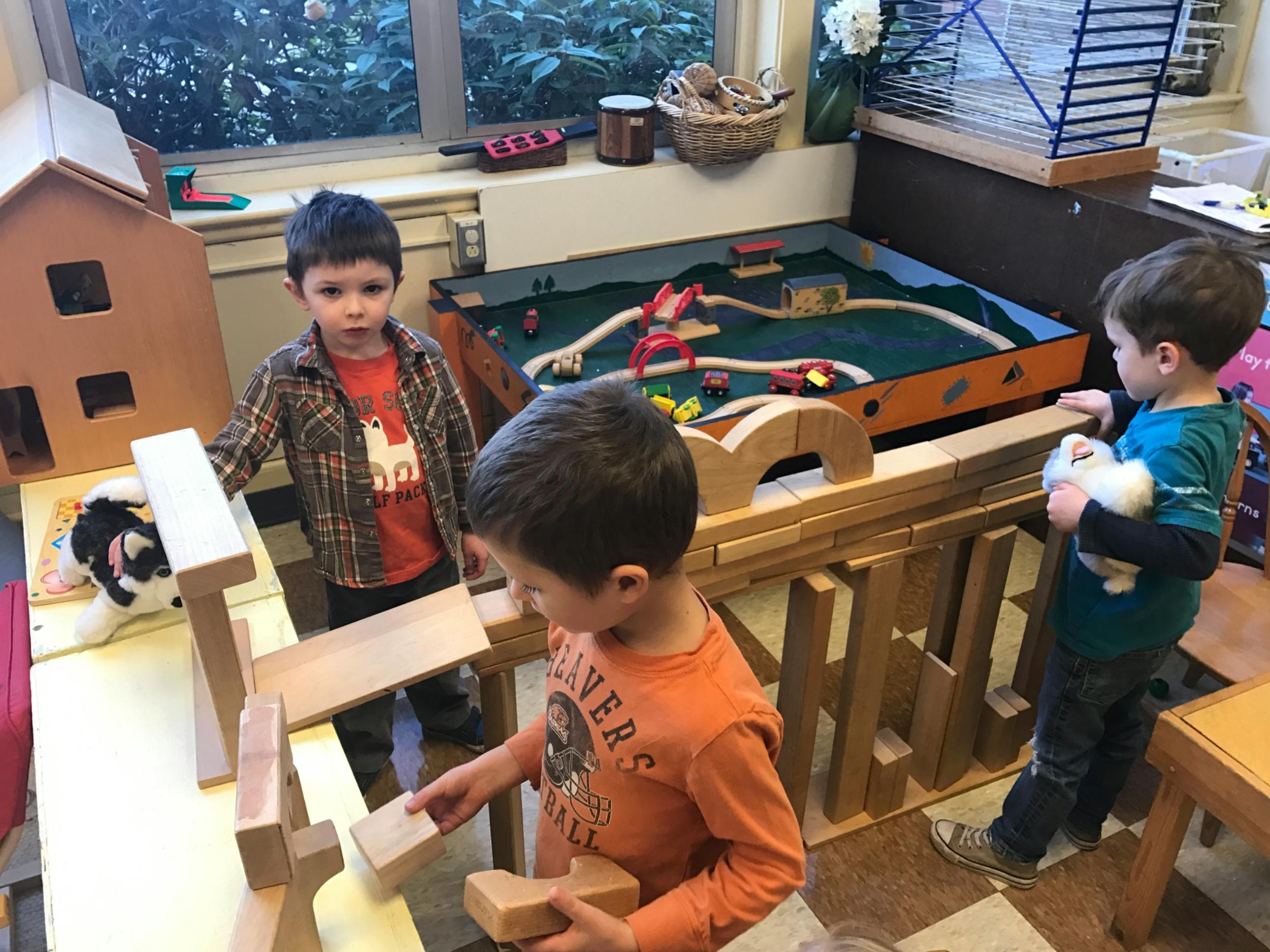 Three children playing with wooden blocks and toys in a classroom