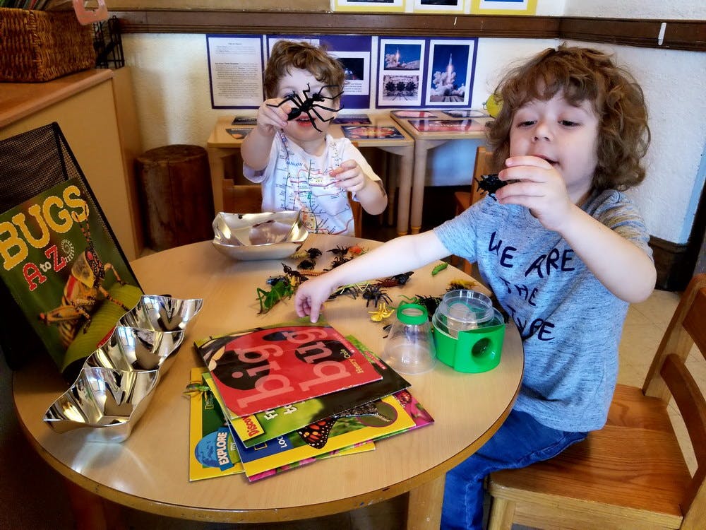 Two children playing with toy bugs at a table