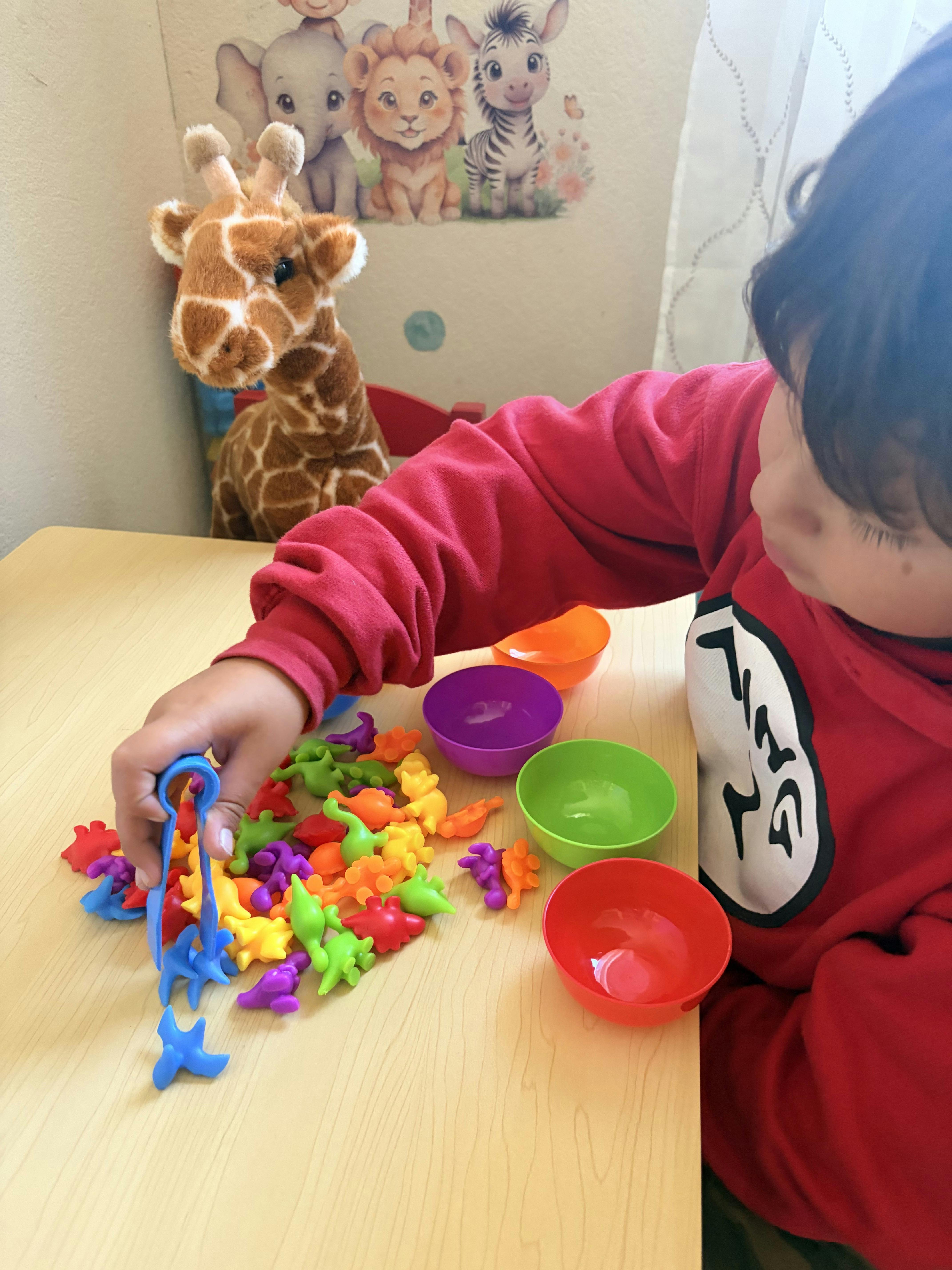 Child using tongs to sort small colorful plastic animals into bowls