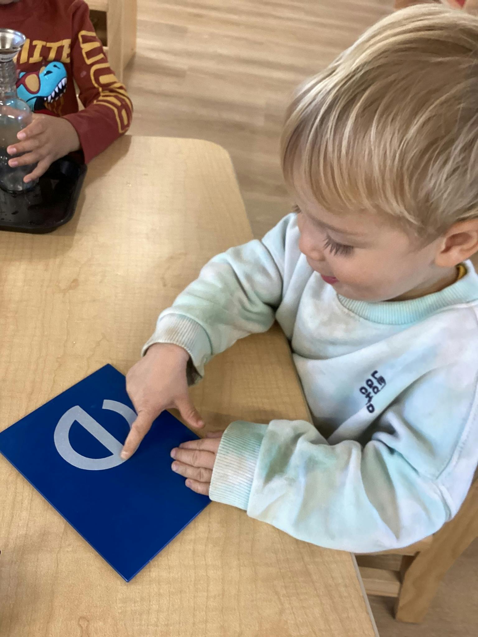Child pointing at a blue card with a white letter 'e' on a wooden table
