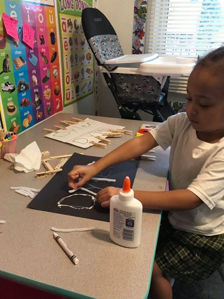 Child gluing pipe cleaners onto black paper at a table