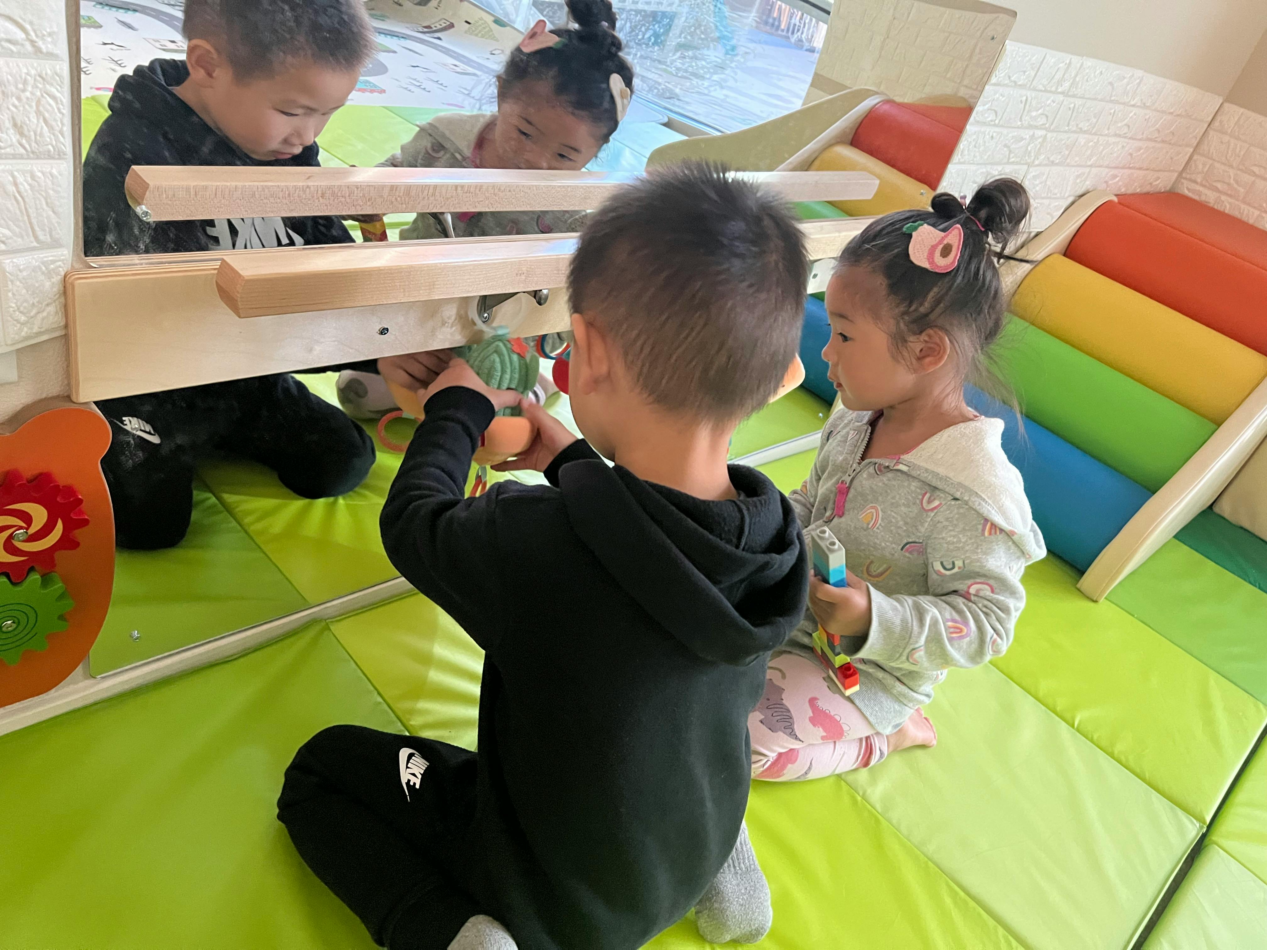 Child playing with a toy in front of a mirror, another child nearby