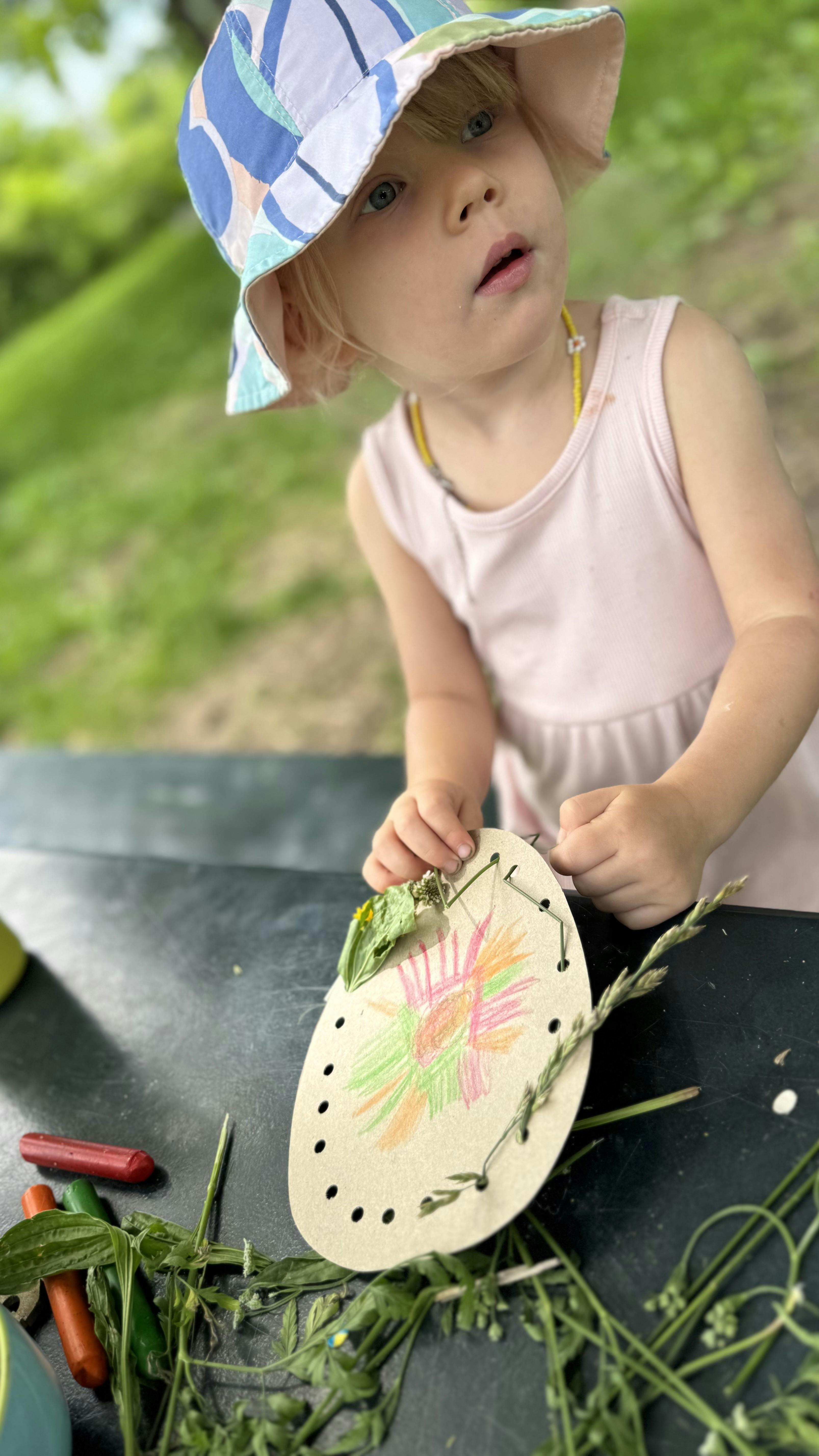 Child crafting with cardboard and natural materials at a table outdoors