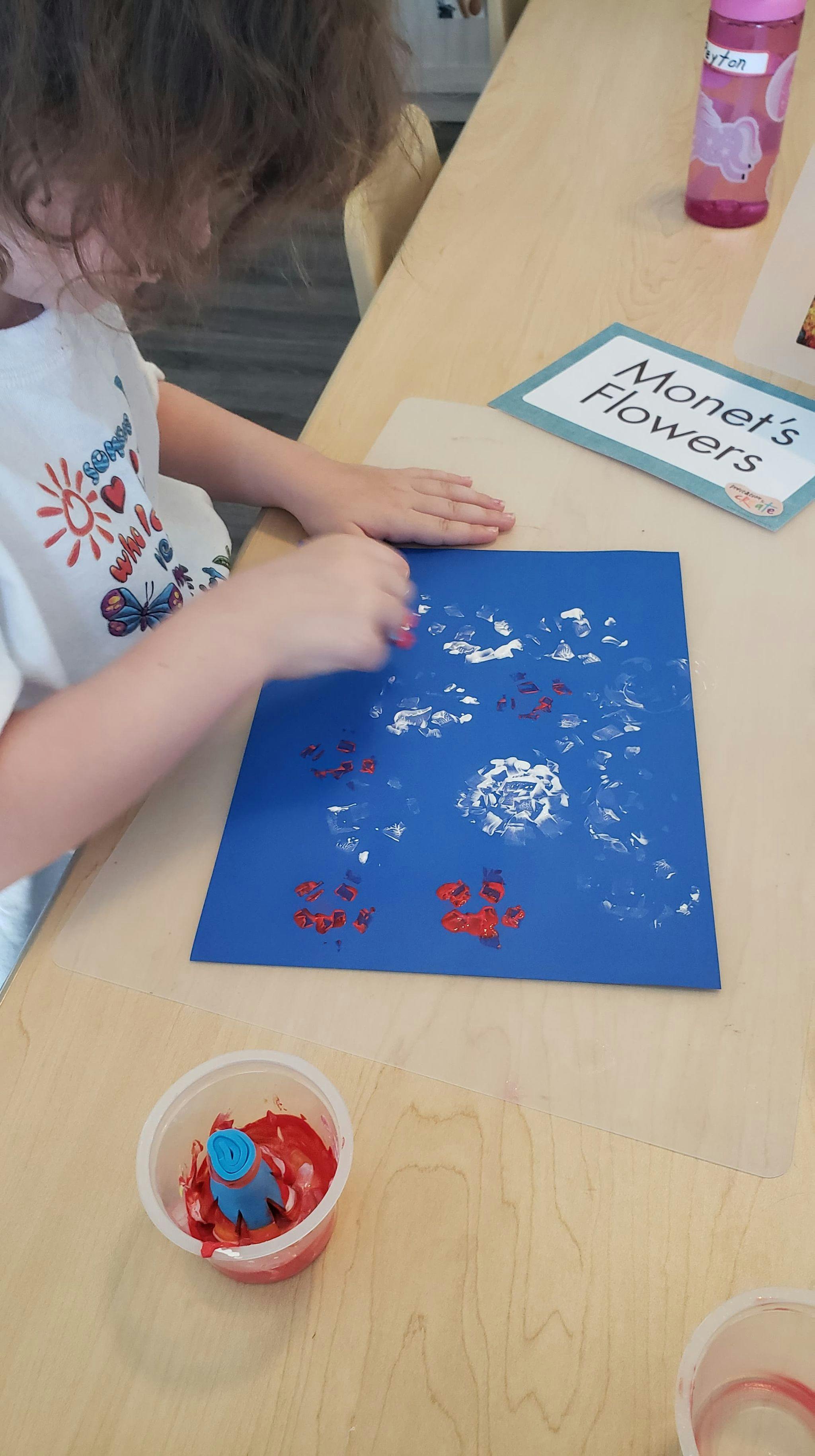 Child painting on blue paper with red and white paint