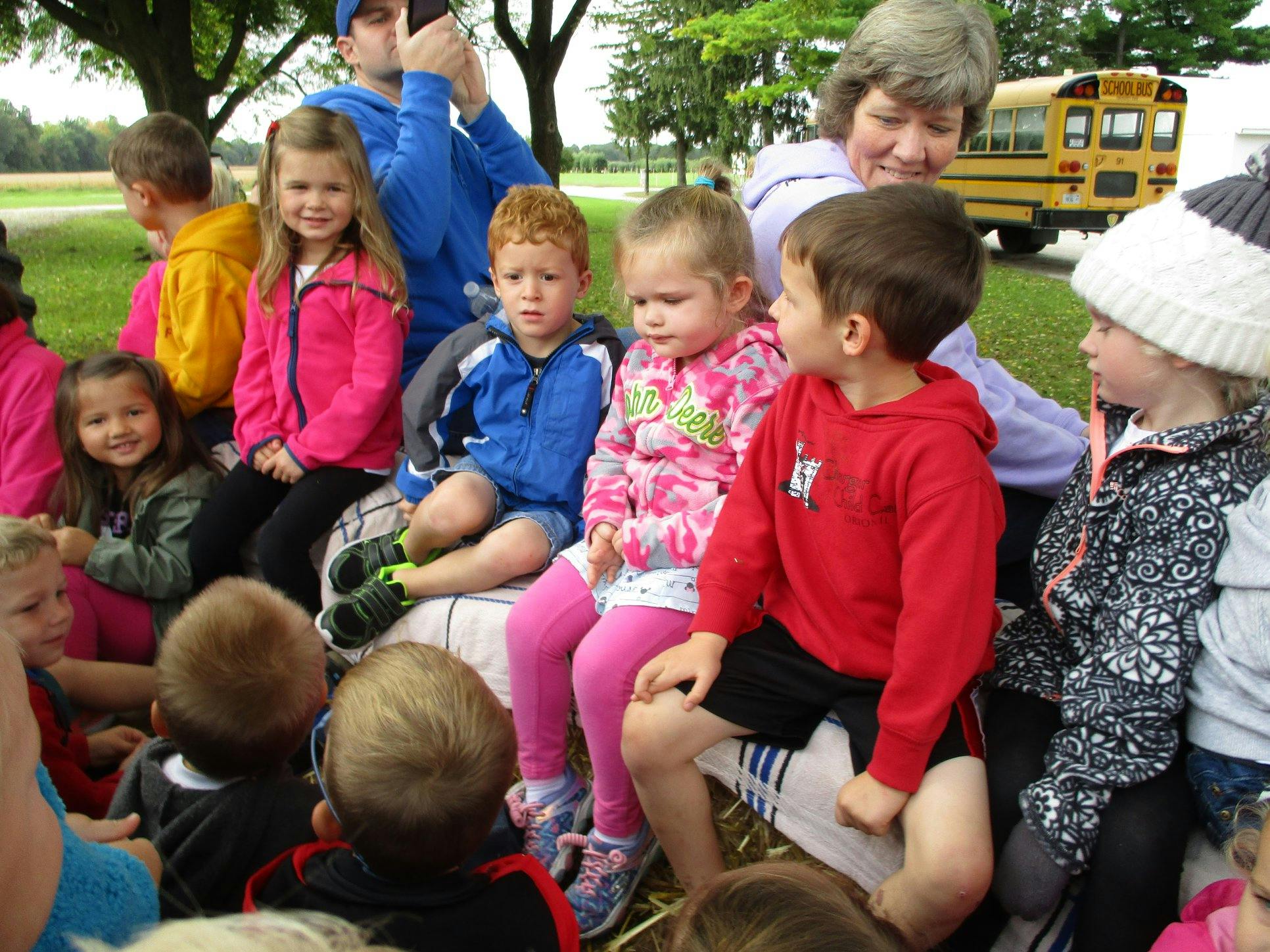 Group of children sitting outdoors, some looking at a person speaking