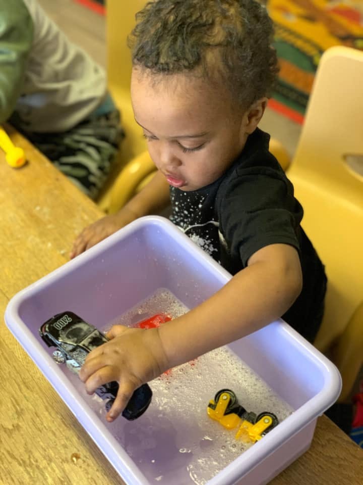 Child playing with toy cars in a bin of soapy water