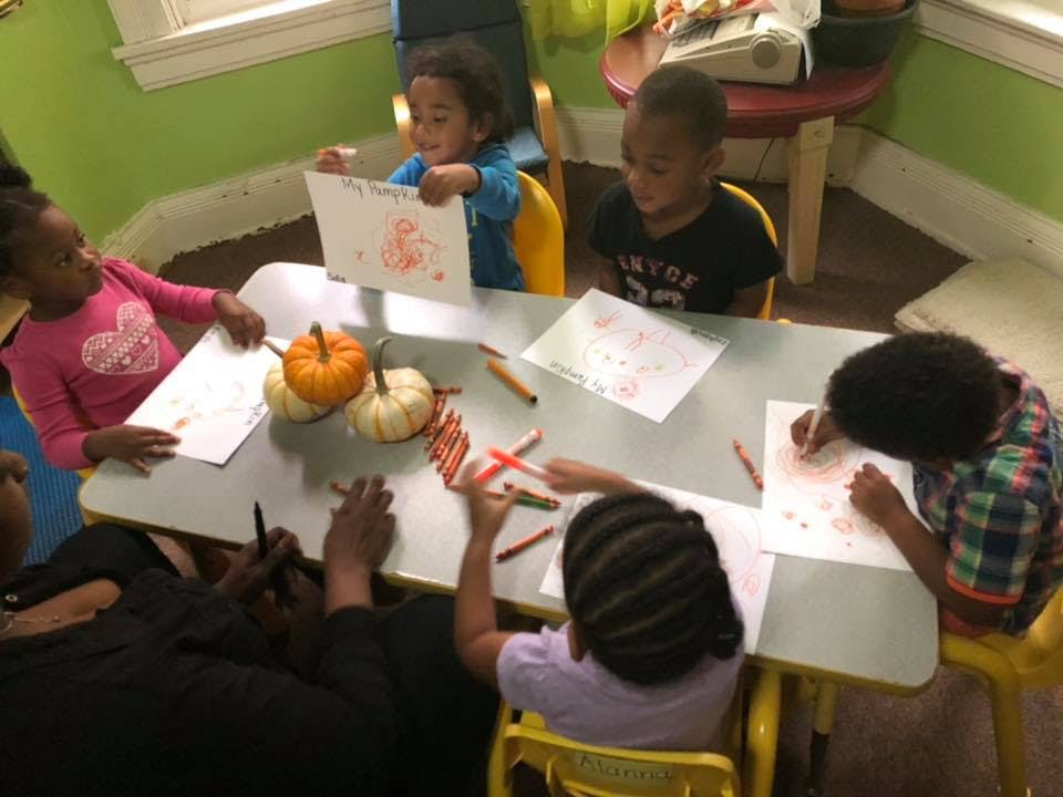 Children drawing at a table with pumpkins