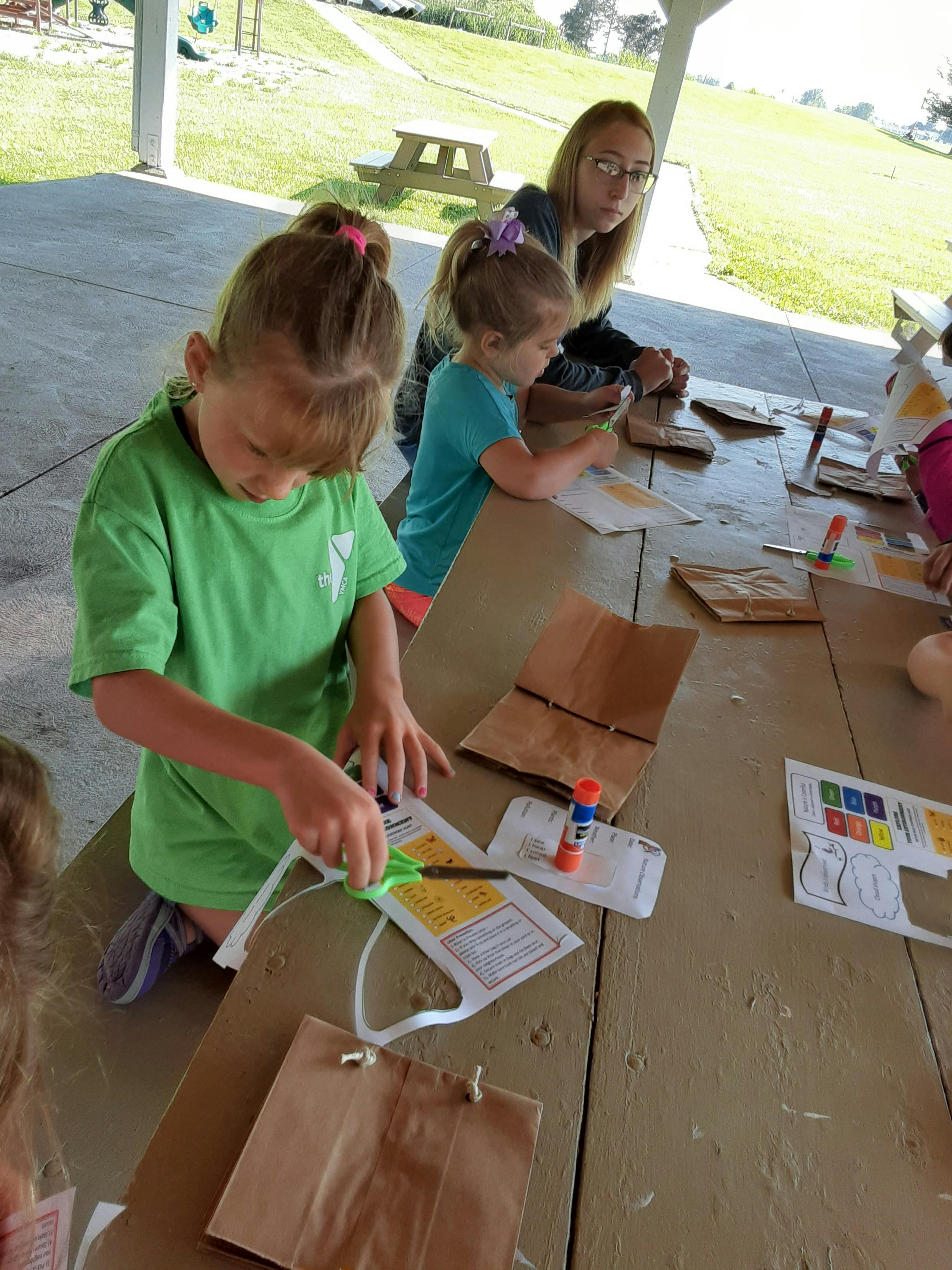 Child cutting paper at a table with other children and an adult
