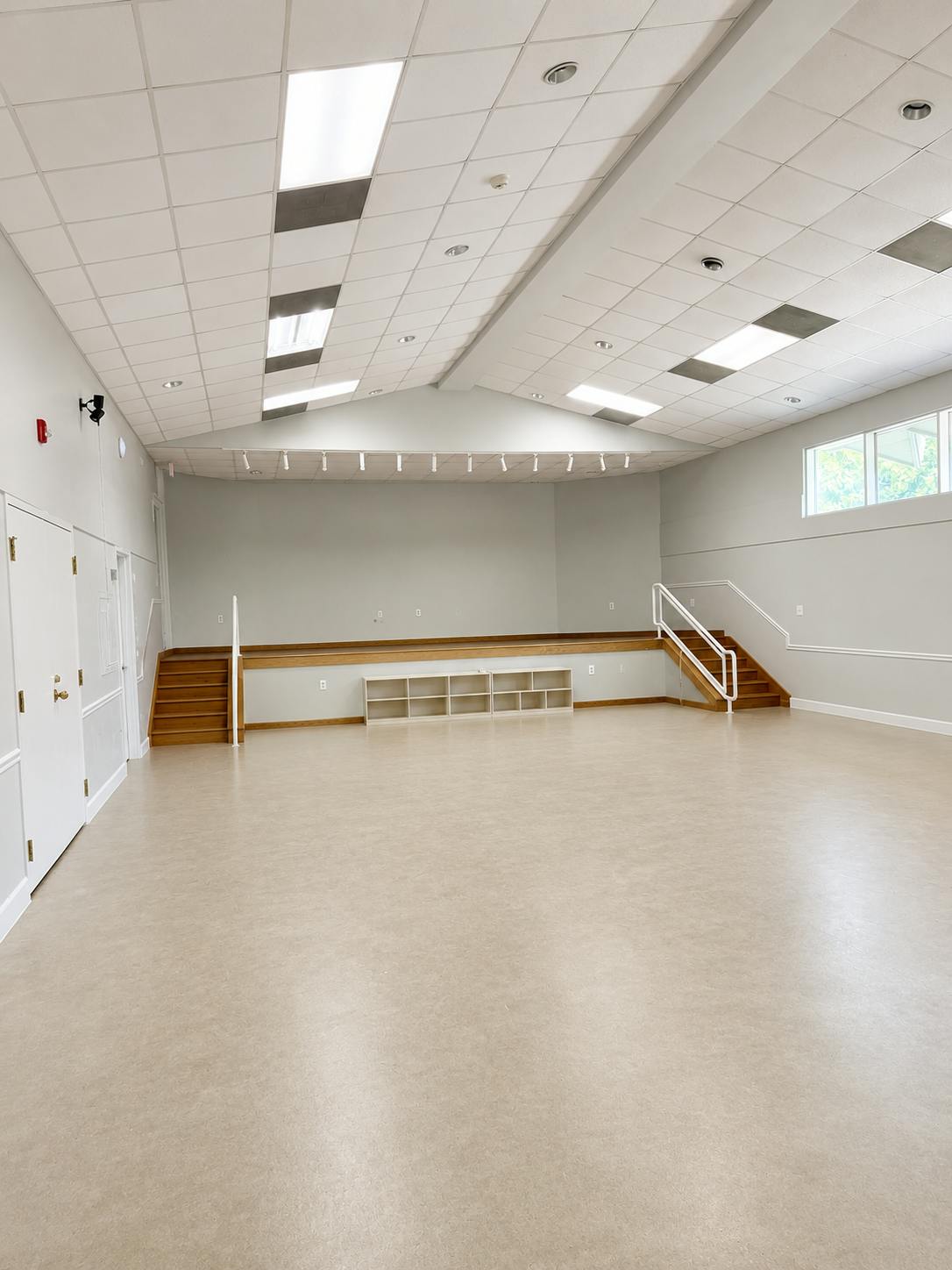Empty multipurpose room with a raised wooden stage and staircase