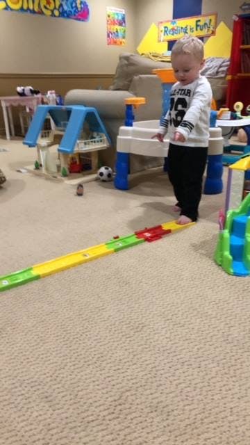 Child standing on a toy car track in a playroom