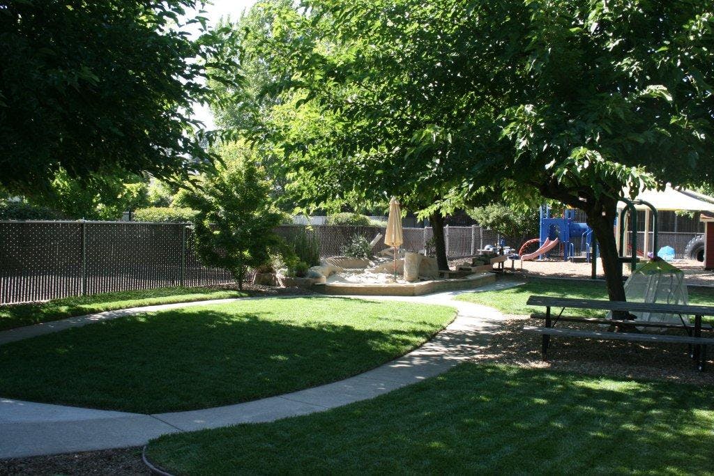 Outdoor playground with grass, trees, and a path leading to play equipment