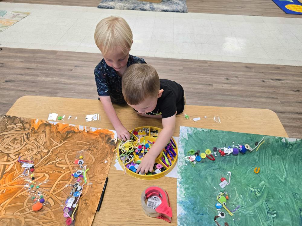 Two children working on art projects at a table in a classroom