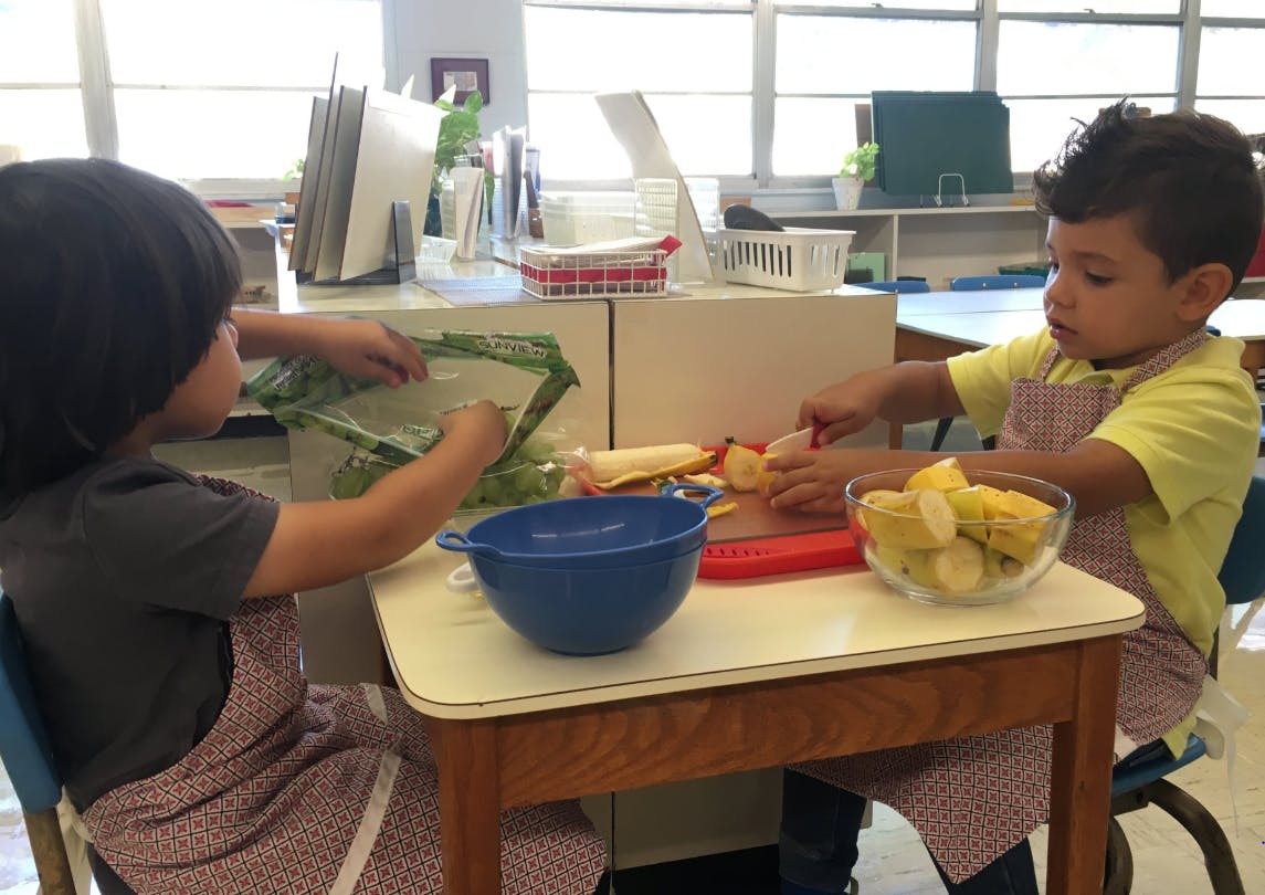 Two children in aprons preparing food at a table