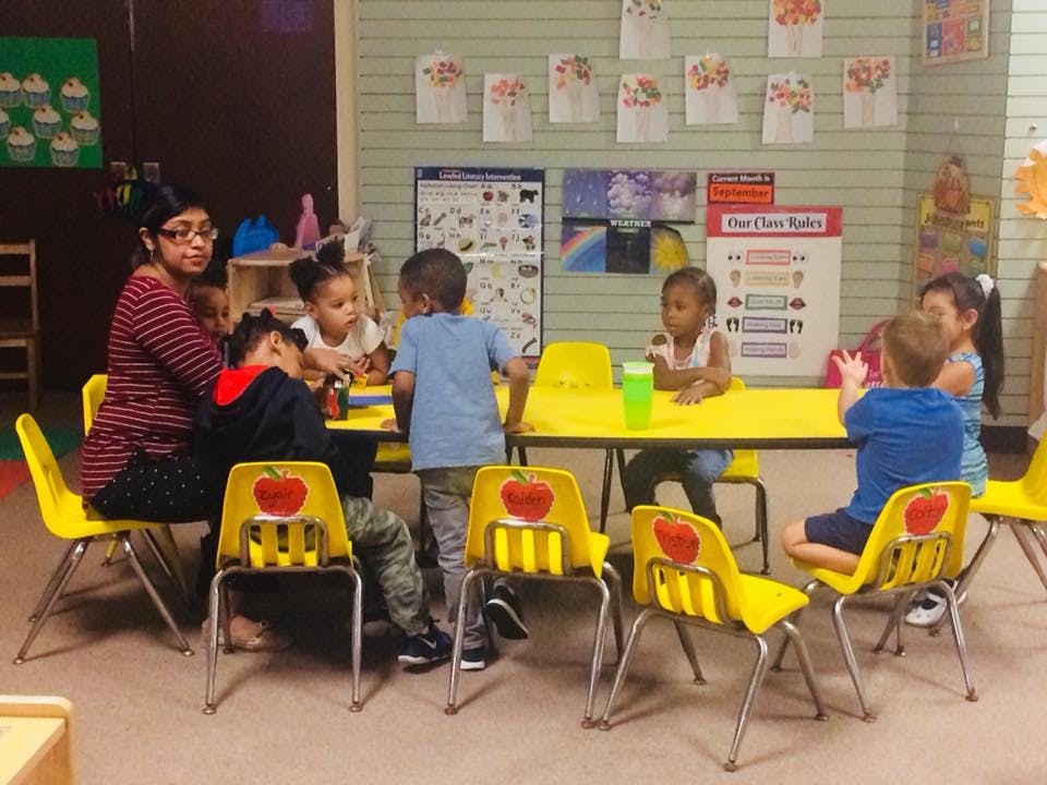 Adult and children sitting at yellow tables in a classroom