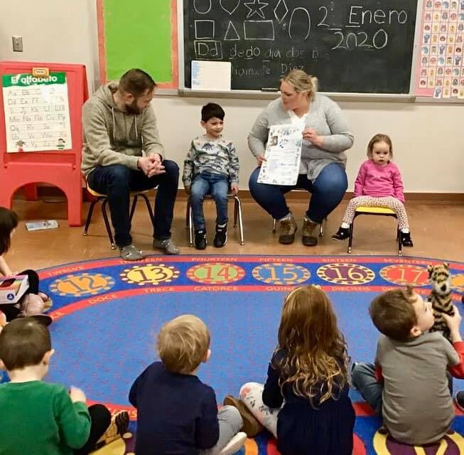 Adults and children sitting in a classroom, some children on the floor