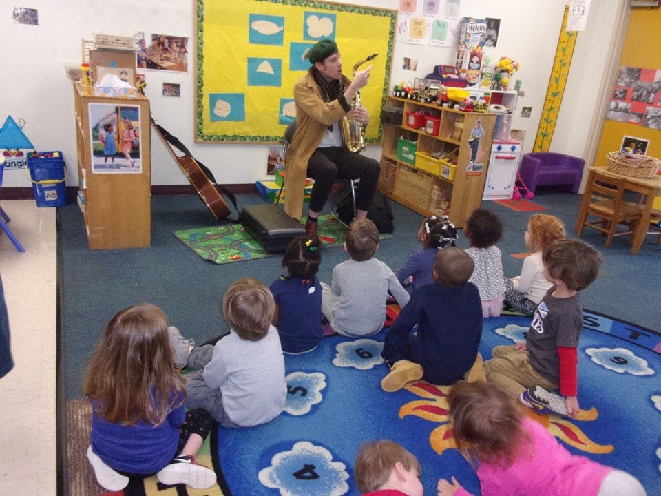 Person playing a stringed instrument for a group of children in a classroom