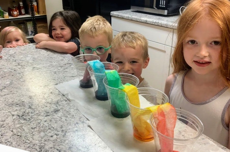 Children watching a science experiment with colorful liquids in cups