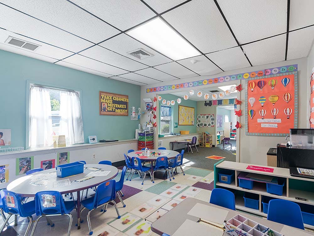 Classroom with small tables and blue chairs, decorated with hot air balloon cutouts
