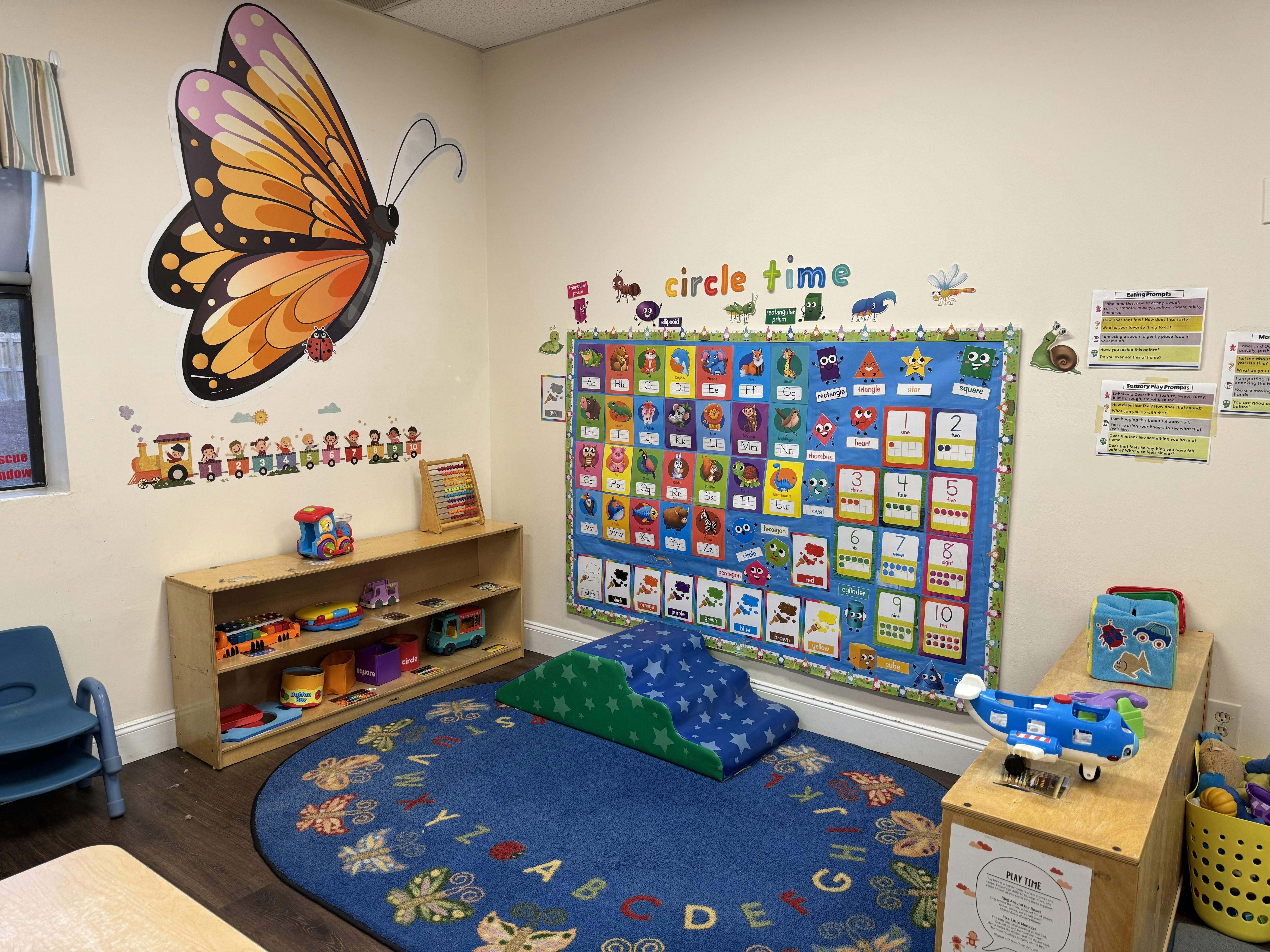 Classroom with a butterfly wall decal, a blue rug, and a bulletin board