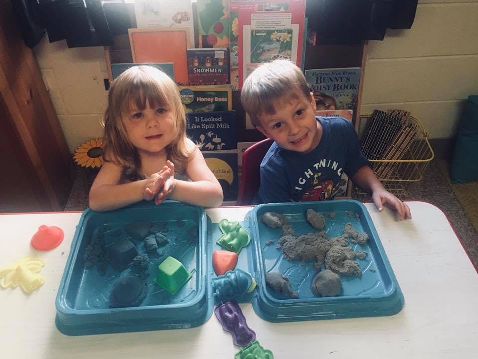 Two children playing with kinetic sand at a table
