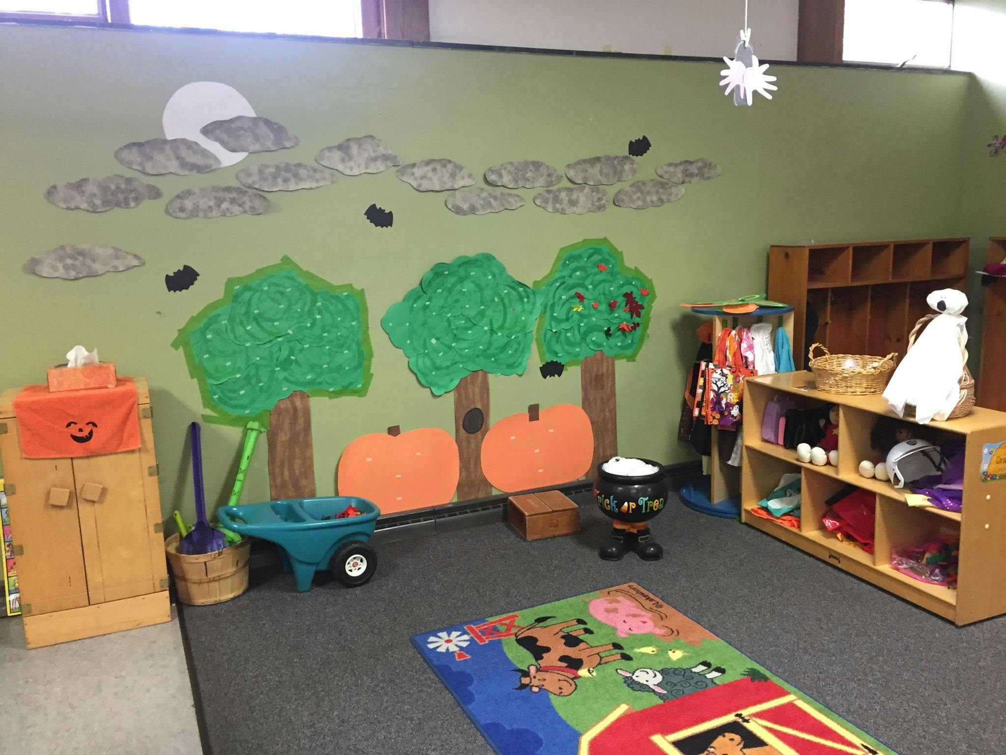 Classroom with wall decorations of trees and pumpkins, shelves, and a rug