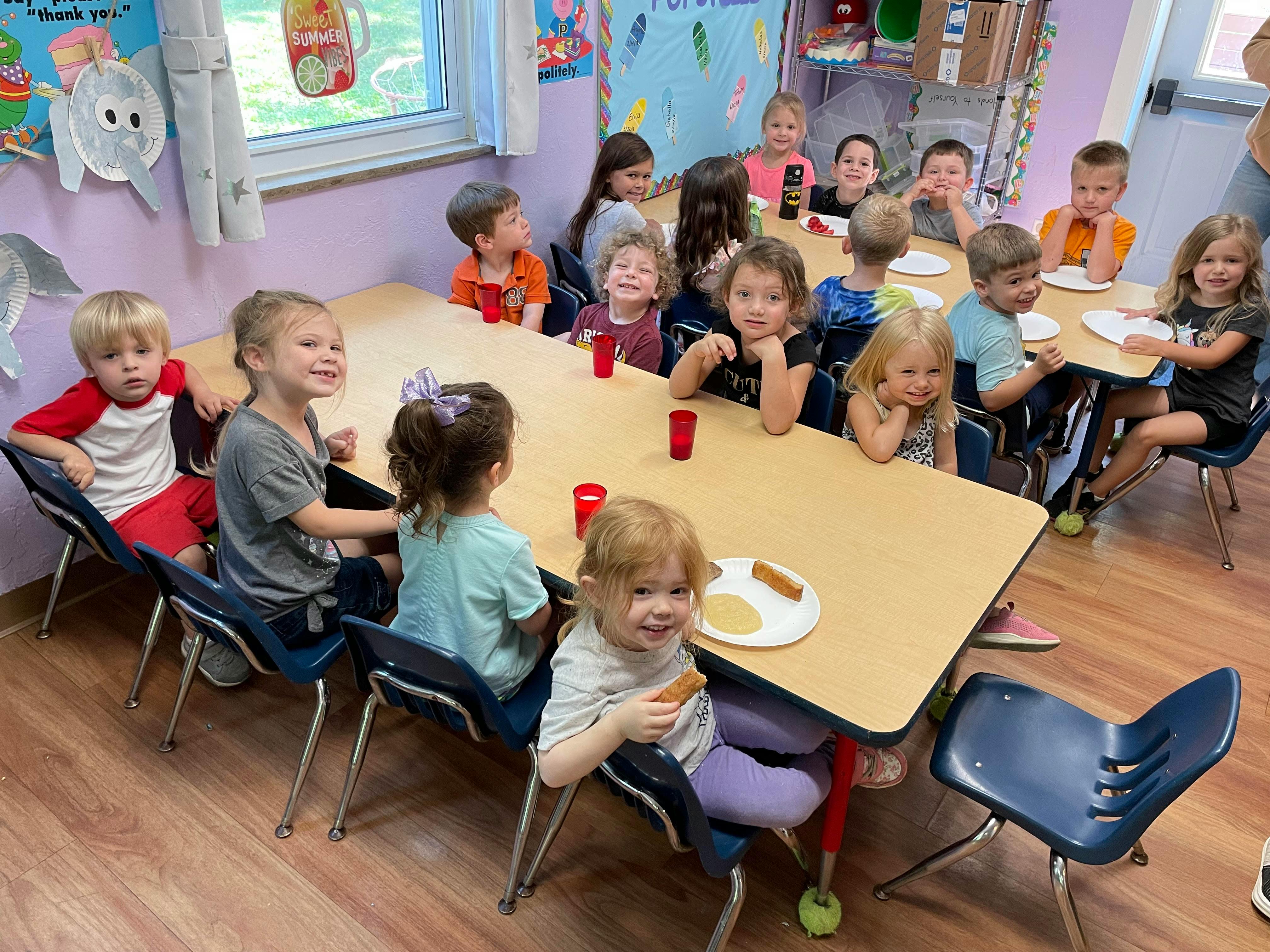 Group of children seated at tables eating snacks in a classroom
