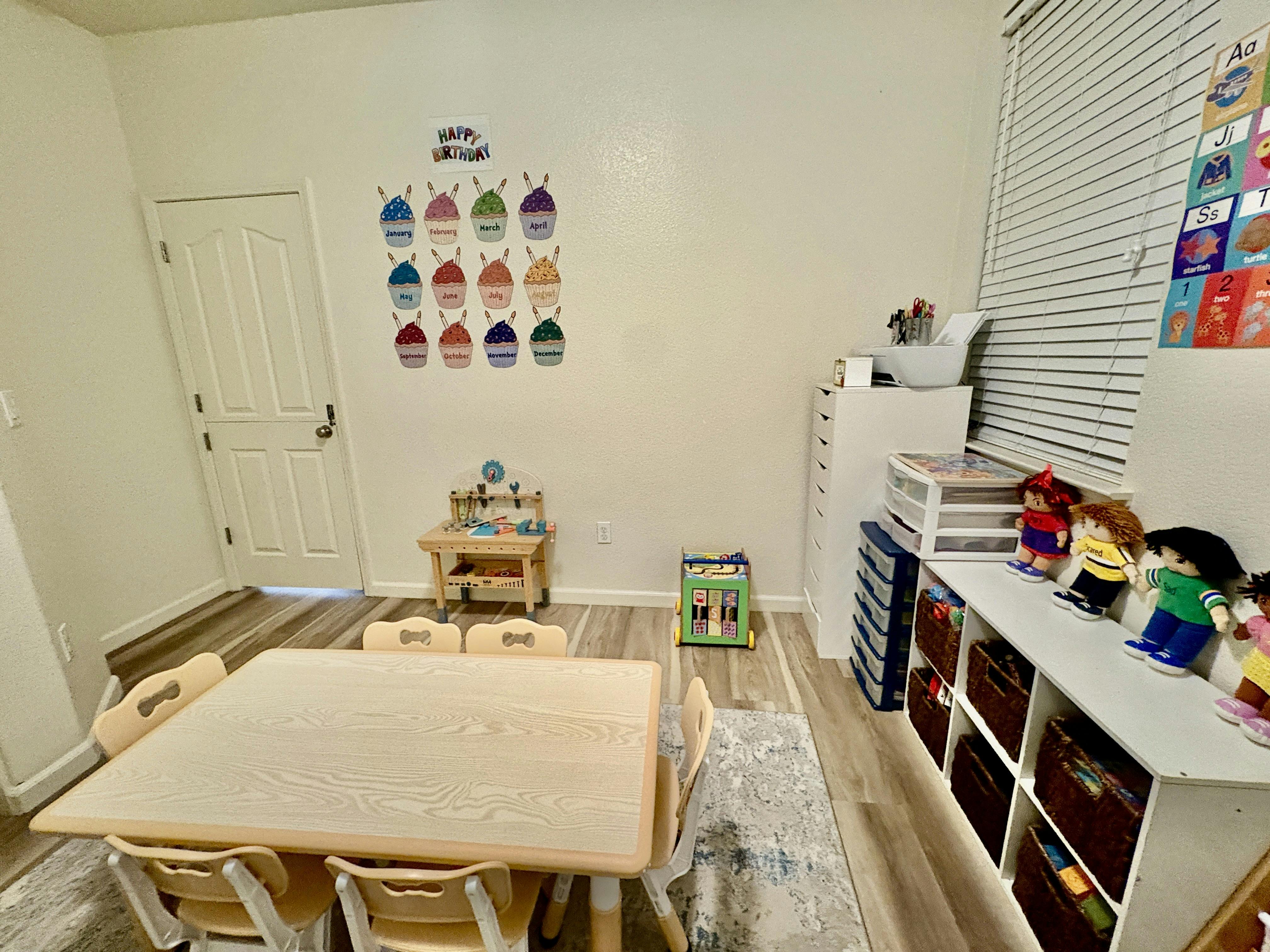 Classroom with a table and chairs, shelves with toys, and a birthday chart