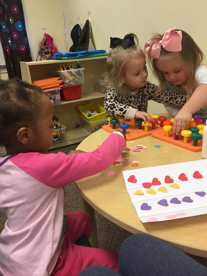 Three children playing with colorful pegboards and heart-shaped cutouts at a table
