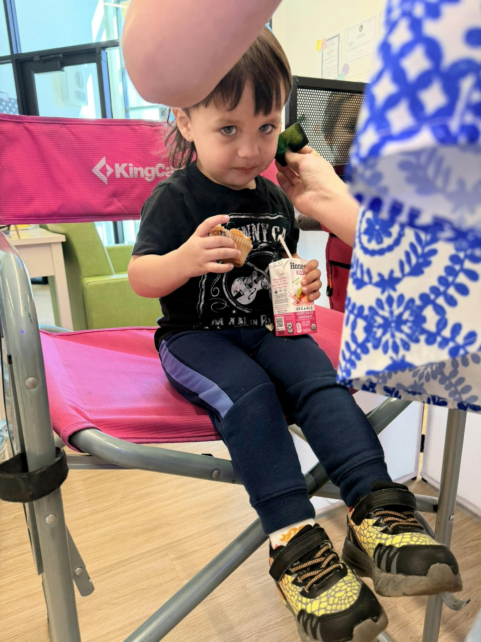 Child sitting in a pink chair holding a juice box and a muffin