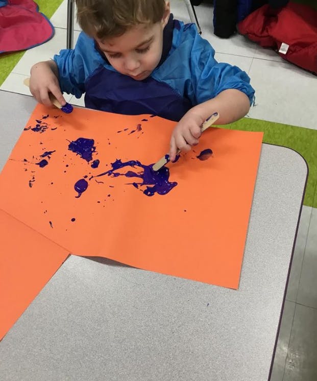 Child painting on orange paper with purple paint