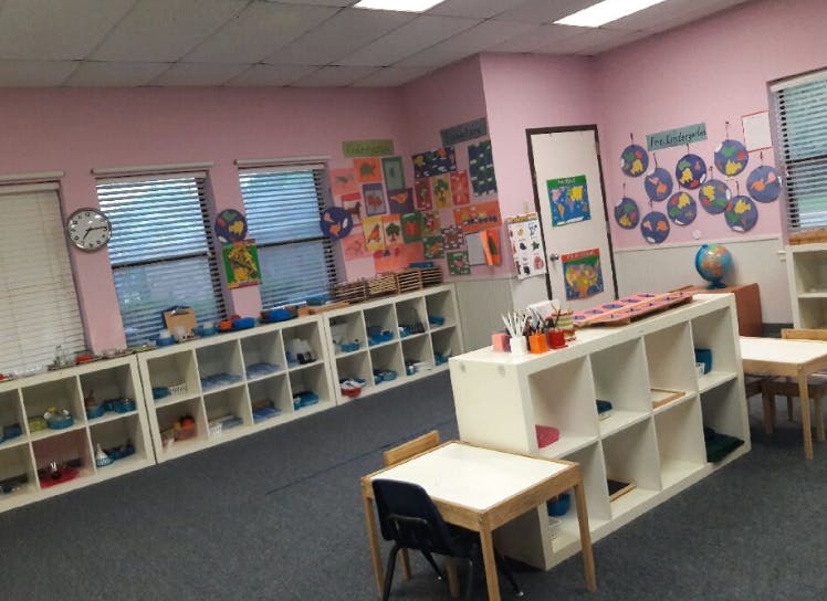 Classroom with pink walls, white shelves, small tables, and chairs