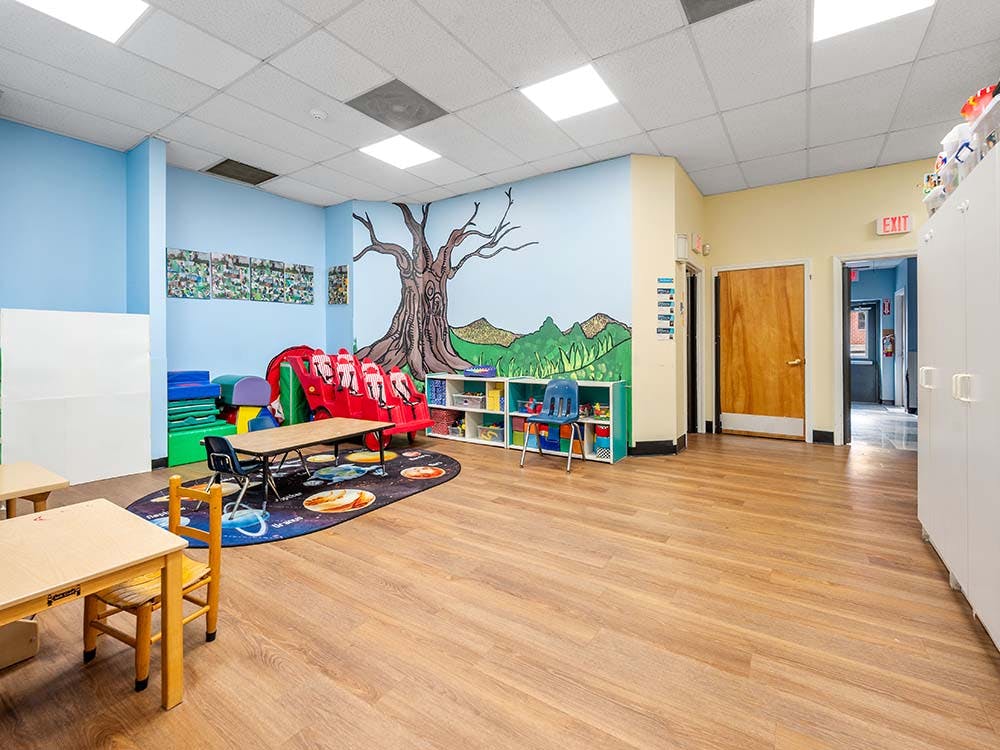 Classroom with child-sized tables and chairs, play area with slide and mural