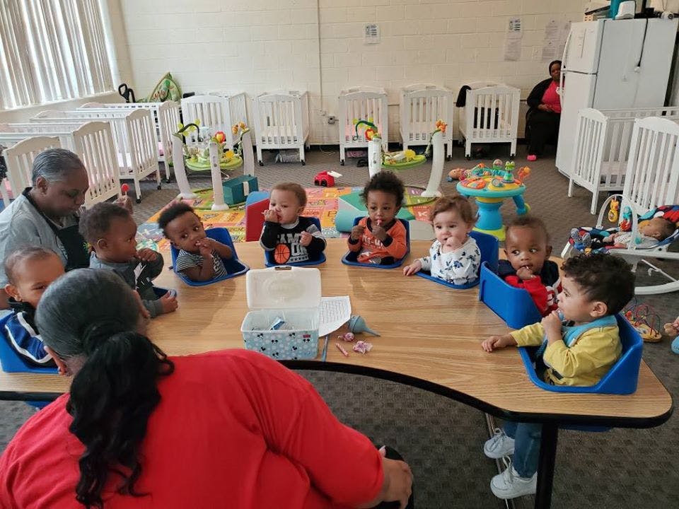Adults and multiple children sitting at a table in a room with cribs