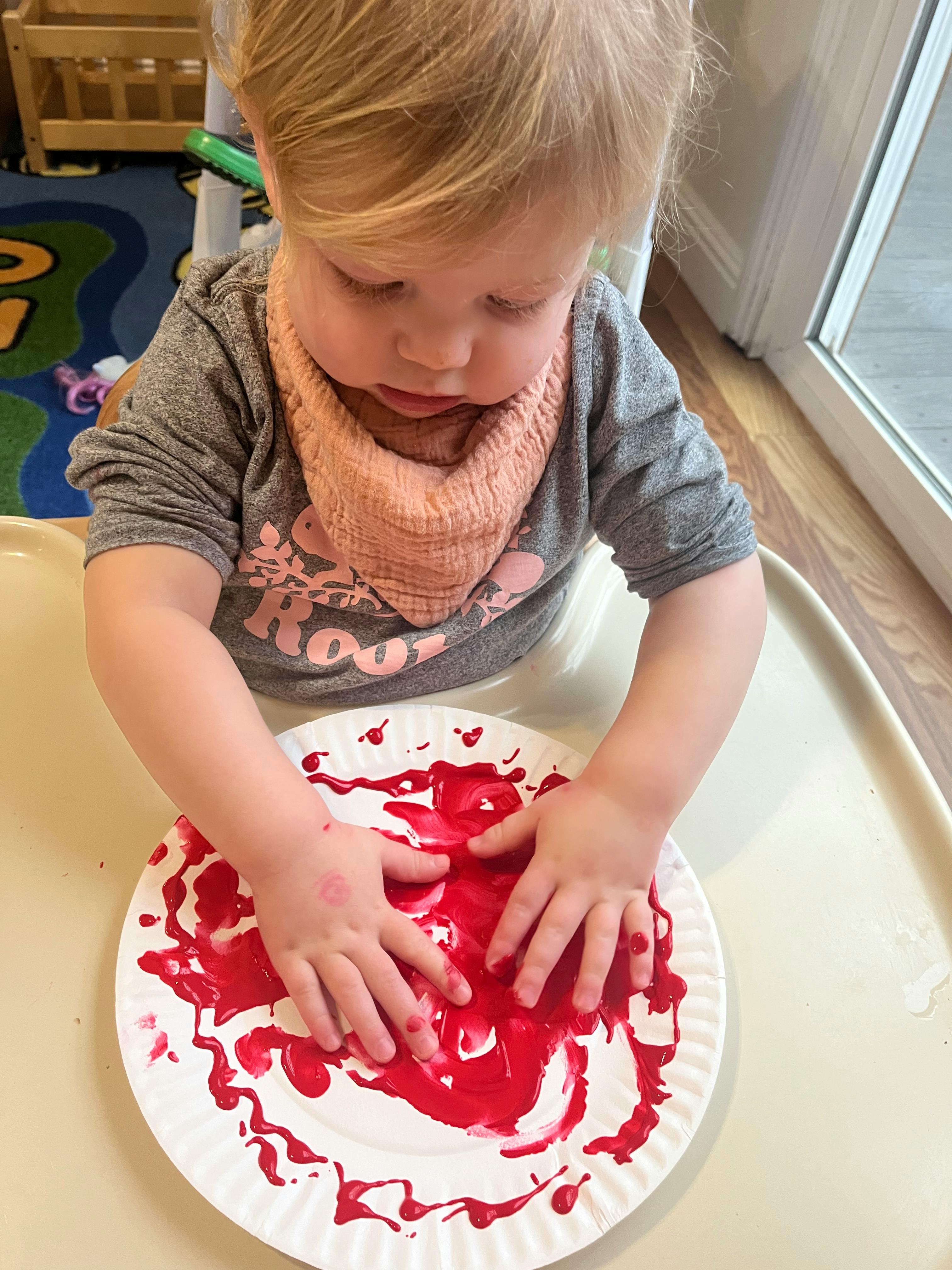 Child with hands in red paint on a paper plate