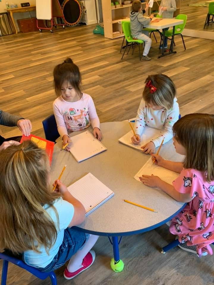 Children sitting at a round table with notebooks and pencils