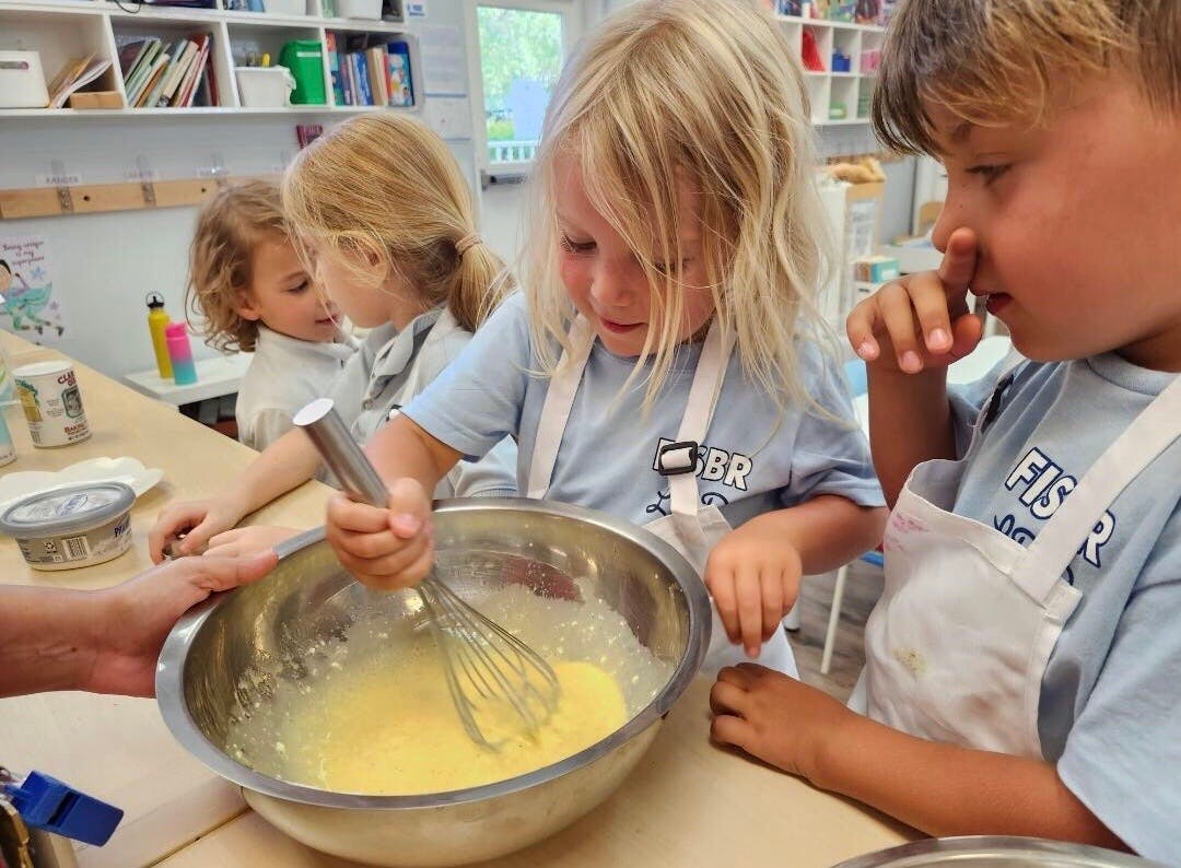 Children in aprons mixing ingredients in a bowl with a whisk