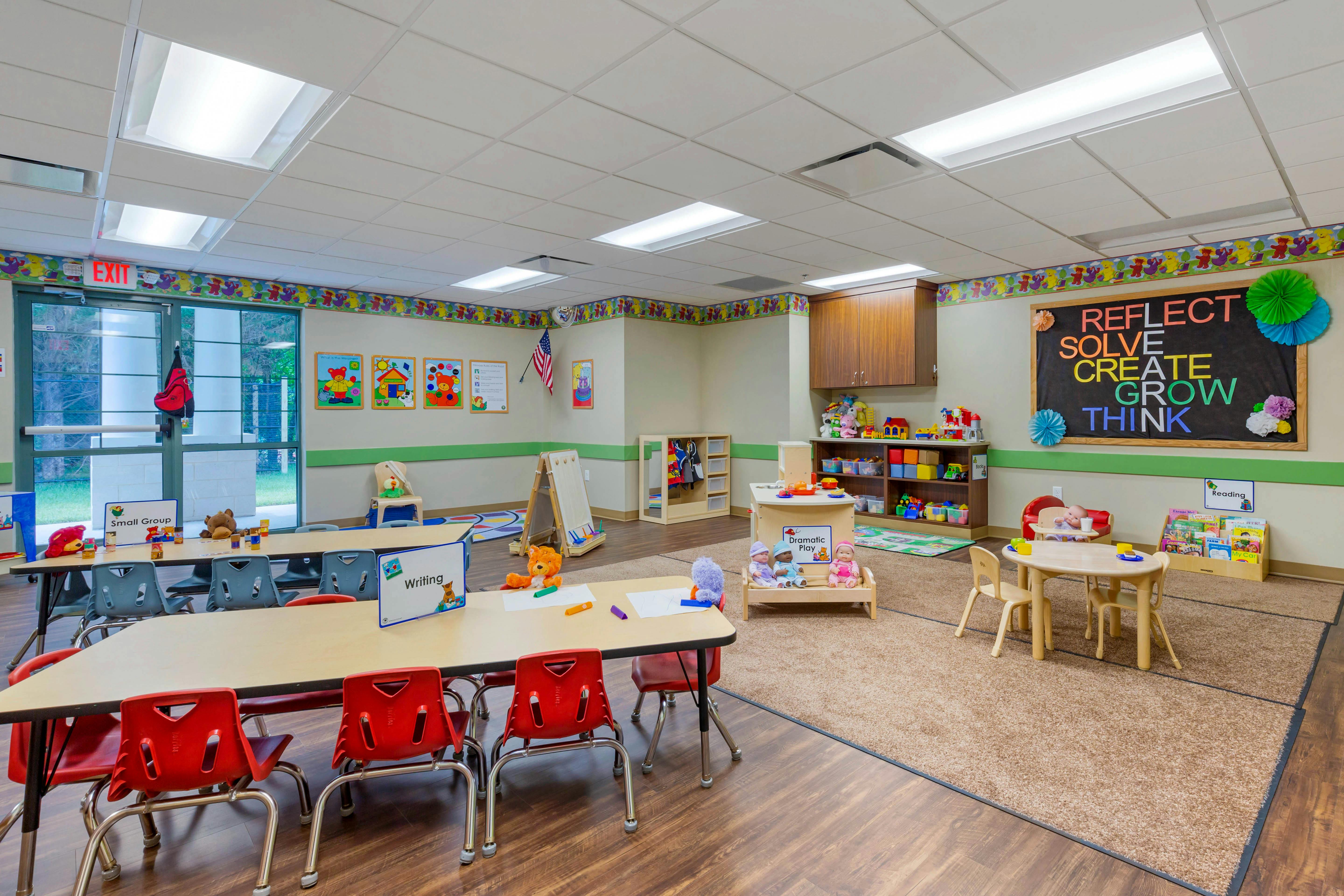 Classroom with child-sized tables and chairs, play kitchen, and a blackboard with words