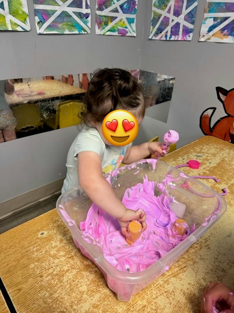 Child playing with purple foam in a plastic bin