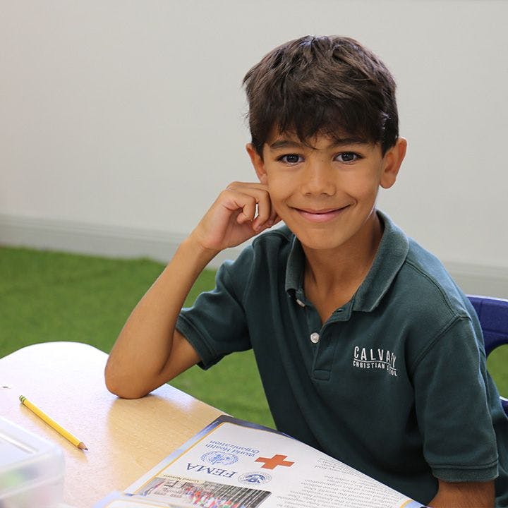 Child in a polo shirt sitting at a desk with an open book