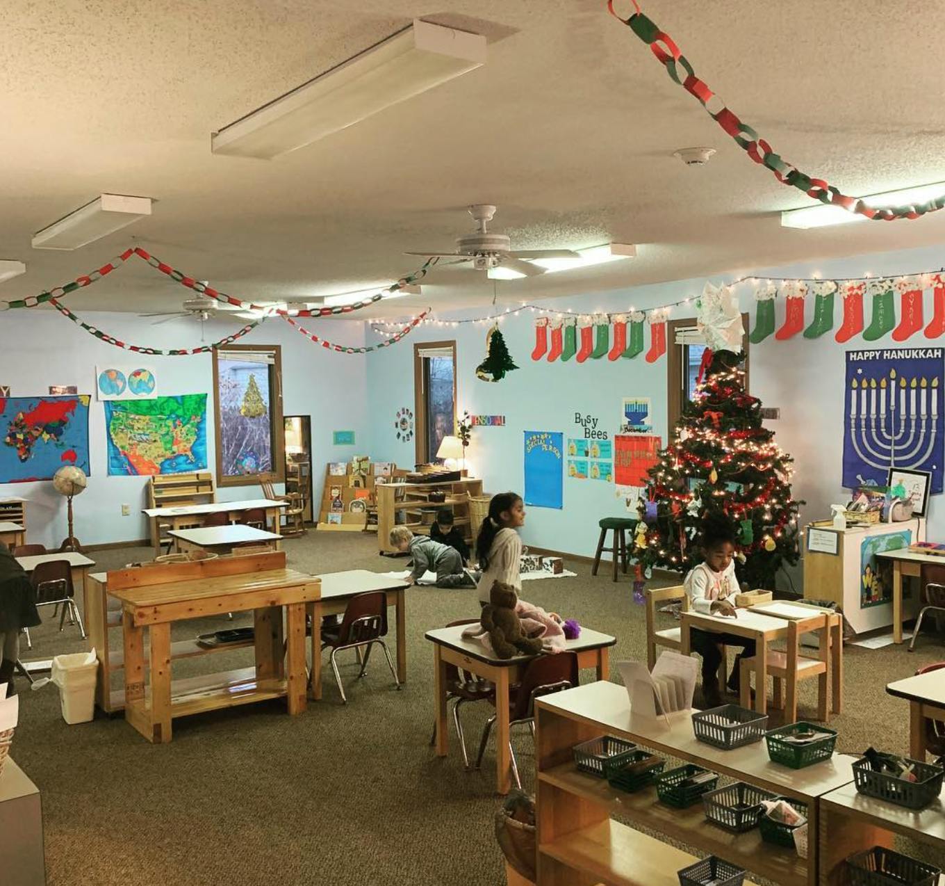 Children in a classroom with a decorated Christmas tree and holiday decorations