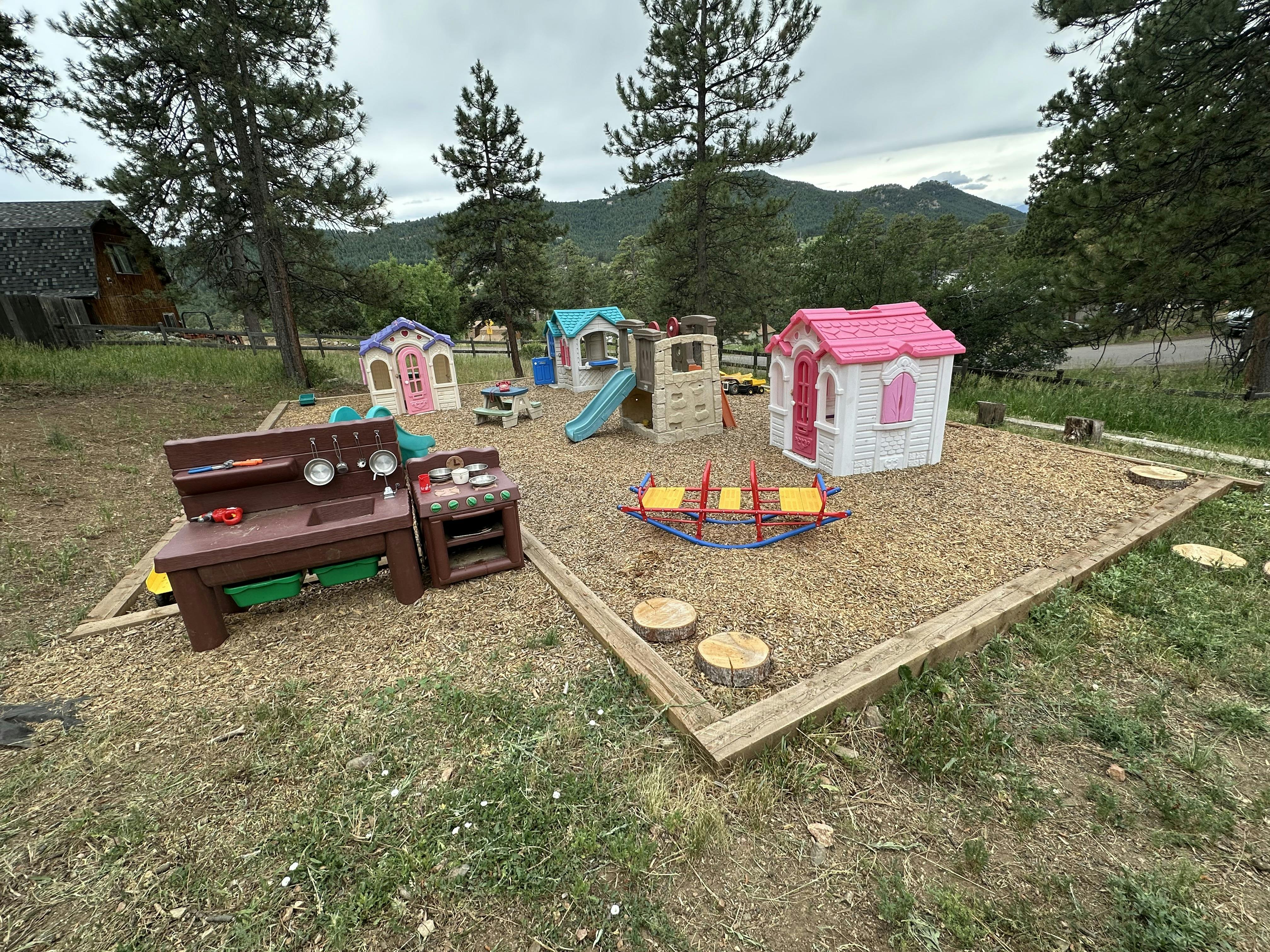 Outdoor playground with playhouses, slide, and seesaw on wood chips