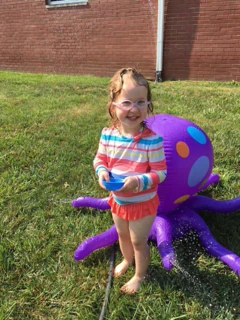 Child in glasses holding a bowl next to an inflatable octopus sprinkler