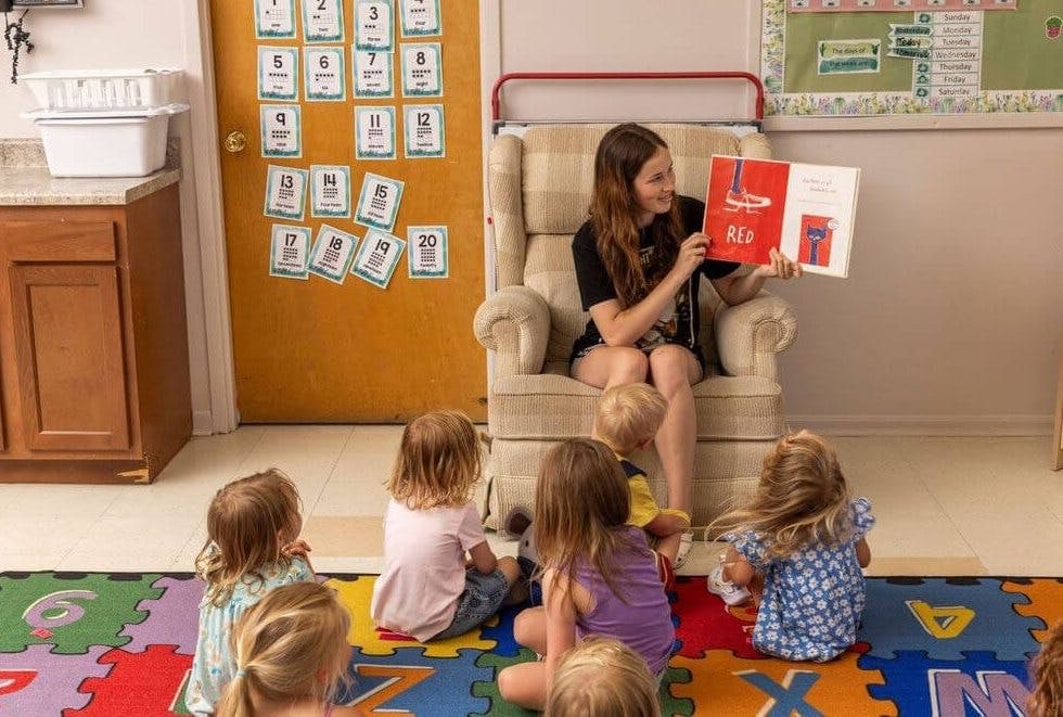 A person sitting in a chair reading a book to a group of children