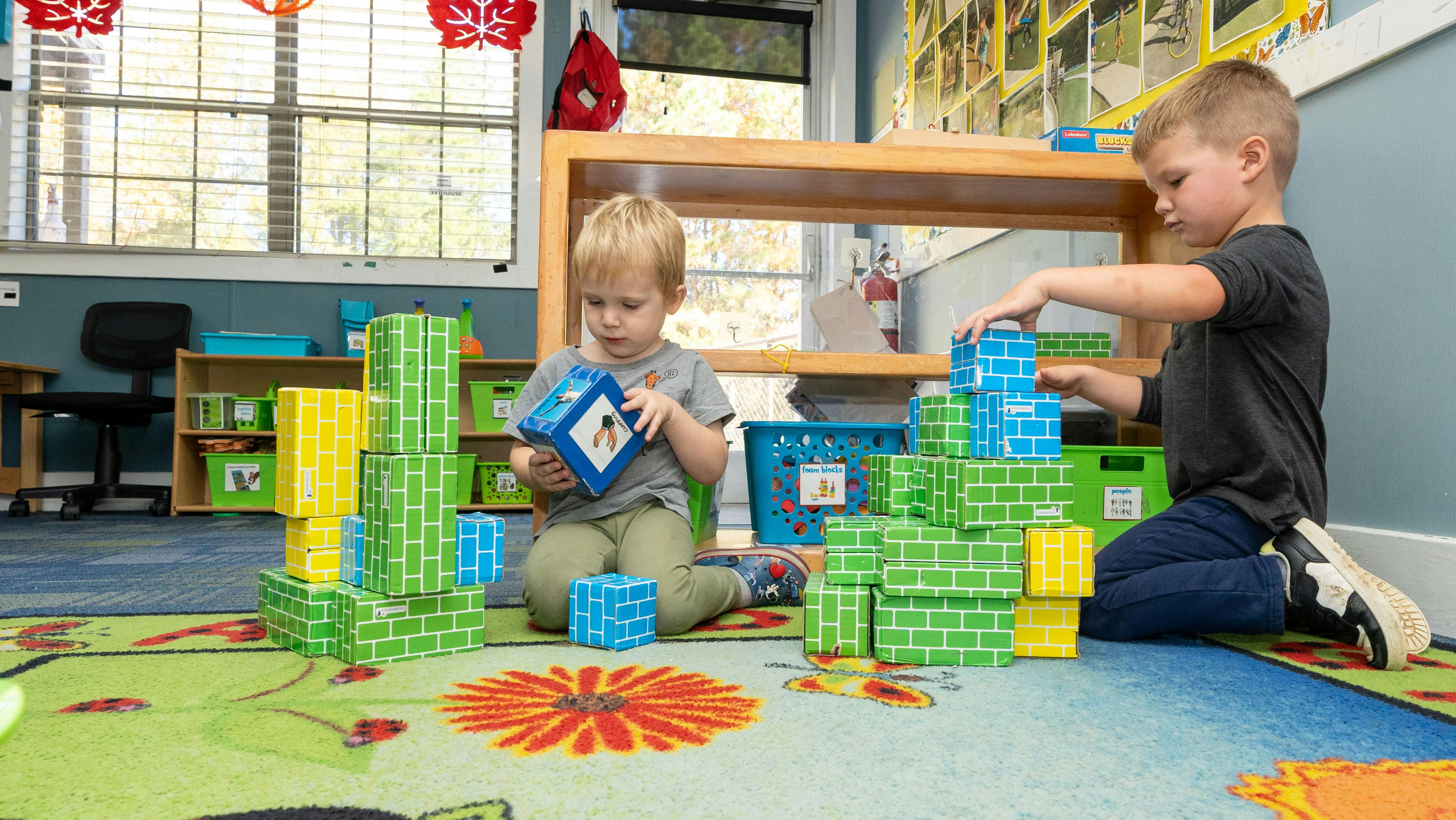 Two children playing with building blocks on a colorful rug
