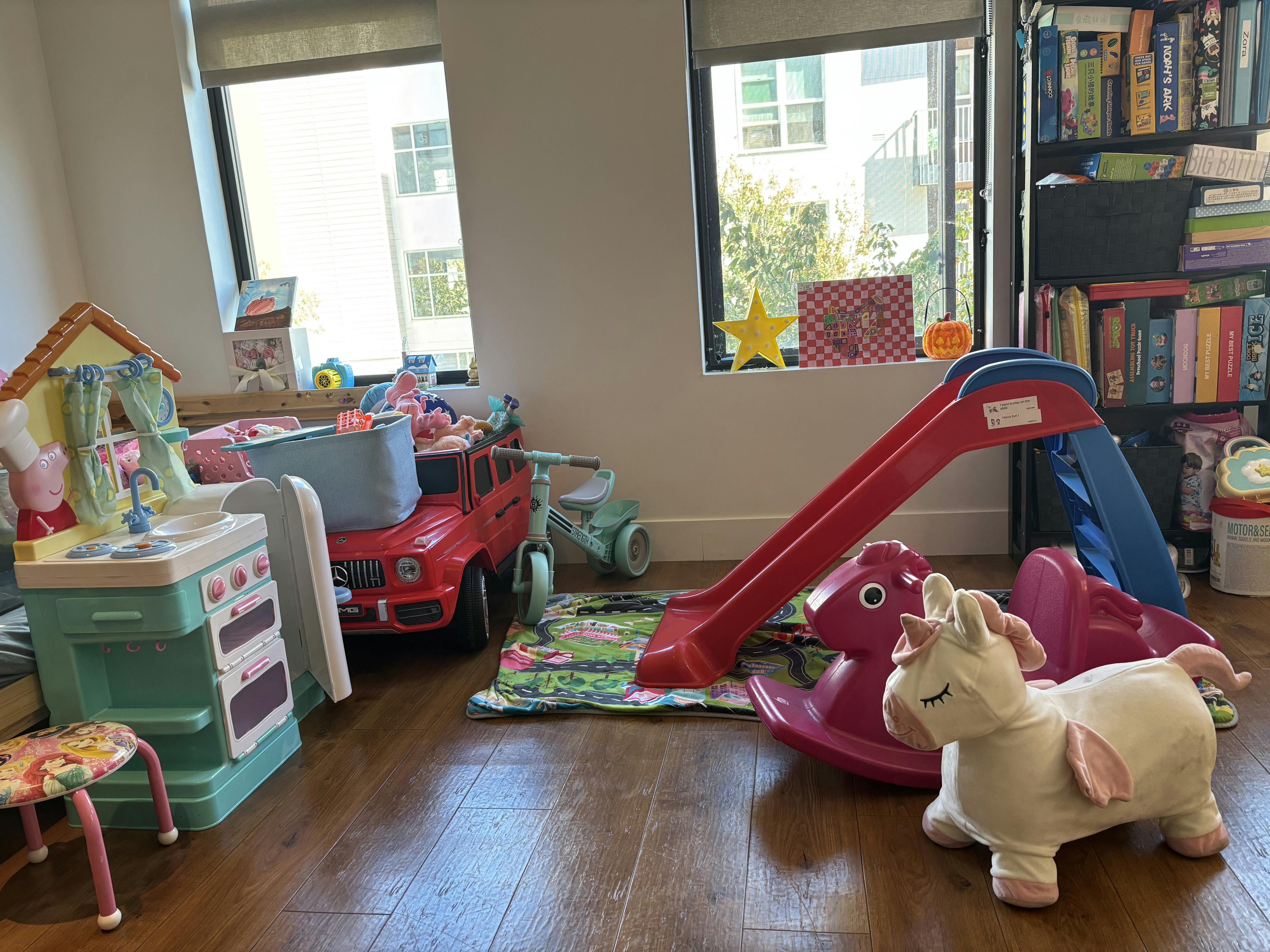 Playroom with toy kitchen, red toy car, red slide, and unicorn ride-on toy