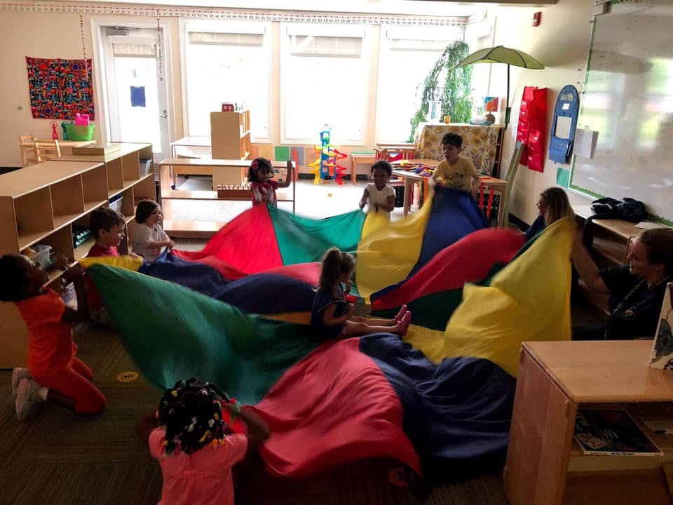 Children playing with a colorful parachute in a classroom