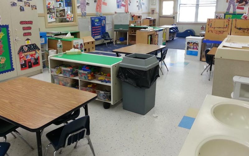 Classroom with tables, chairs, shelving units with toys, and a trash can